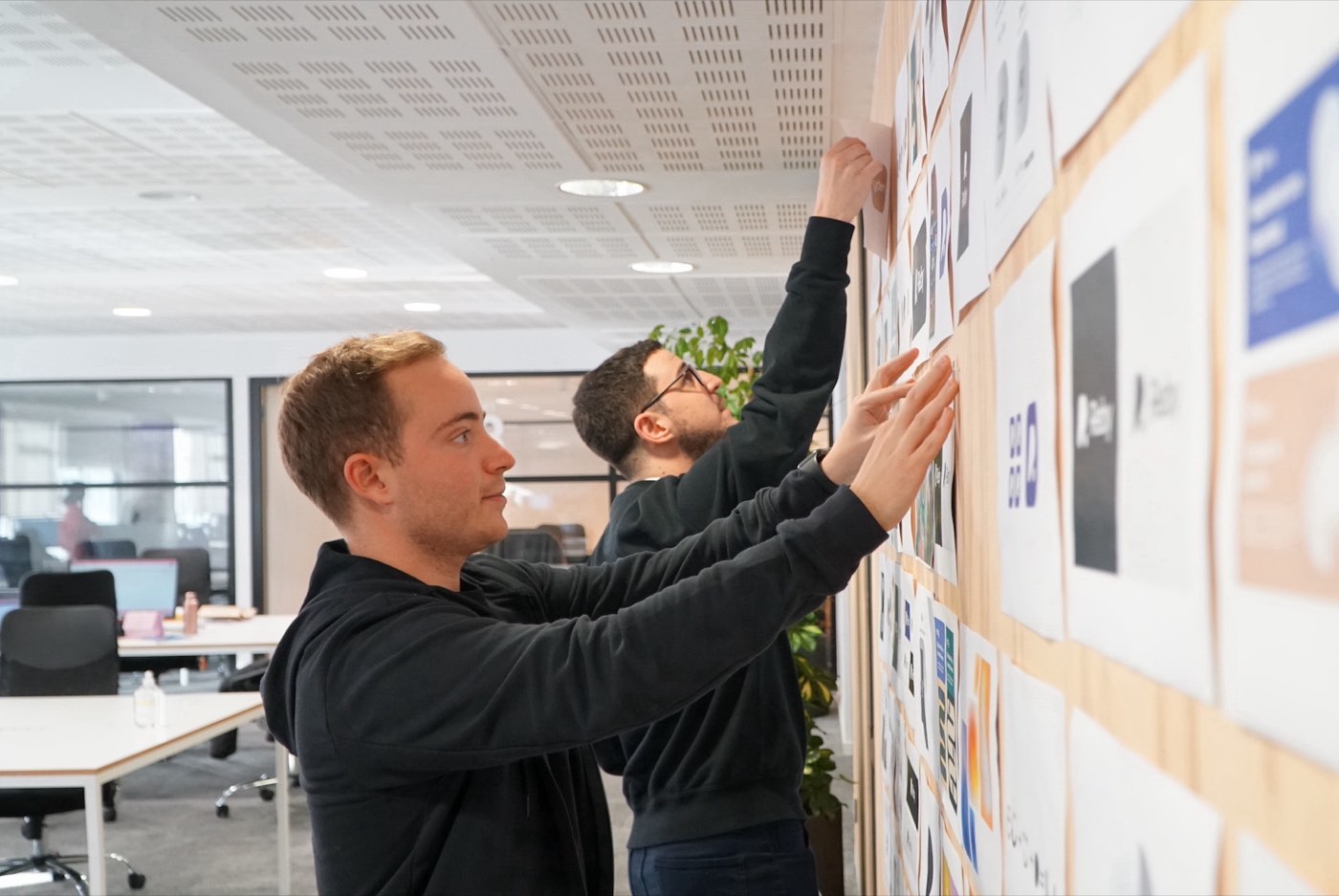 Dos diseñadores colgando exploraciones de marca en una pared, en Bnext